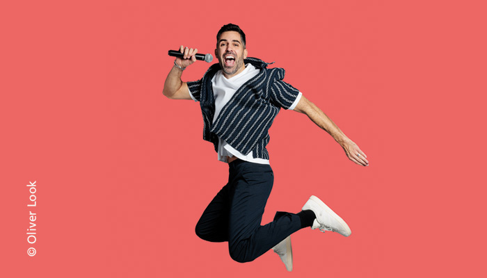 Daniel Luis im Sprung mit Mikro und Nadelstreifen Jacket über weißem T-Shirt zu schwarzer Hose.